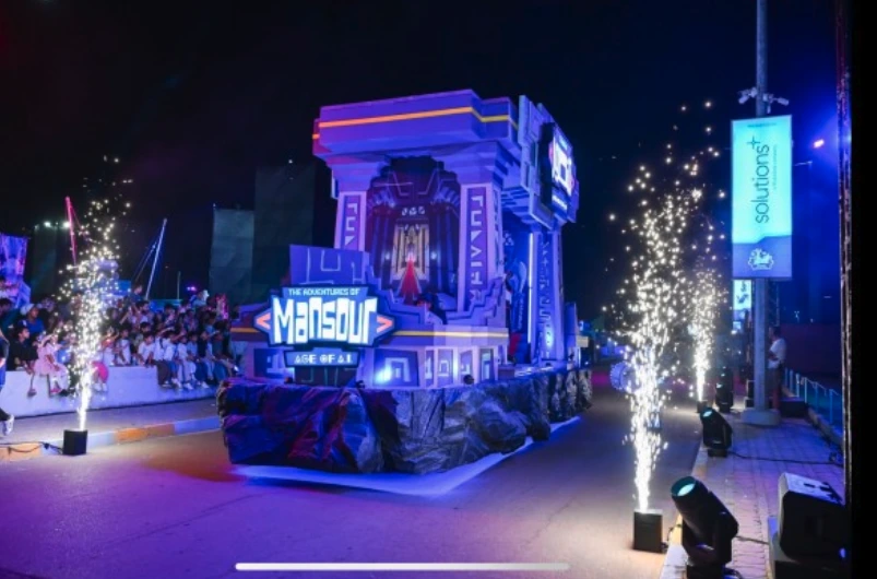 Night-time festival scene showing a large branded float with fireworks effects and crowd presence.